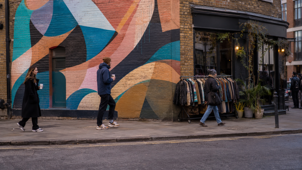 Street corner in Shoreditch East London with a colourful mural, vintage shop and pedestrians near Shoreditch High Street station
