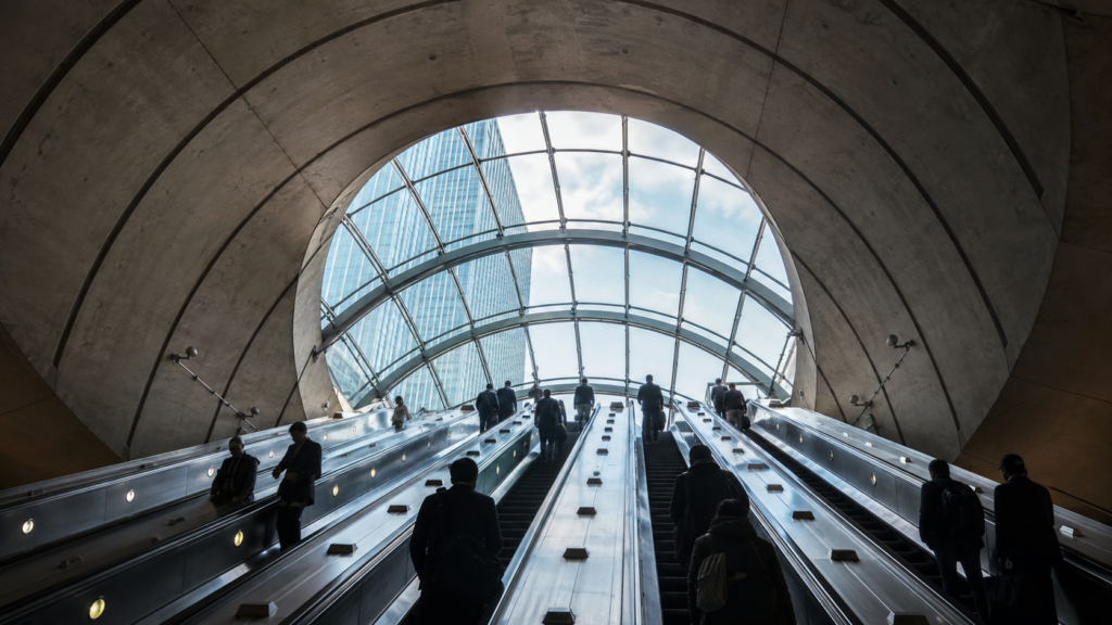 Commuters on the escalators beneath the glass canopy of Canary Wharf Underground station